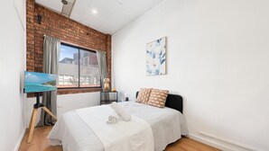 A bedroom with a bed, a painting, a window with curtains, and a wall-mounted picture.