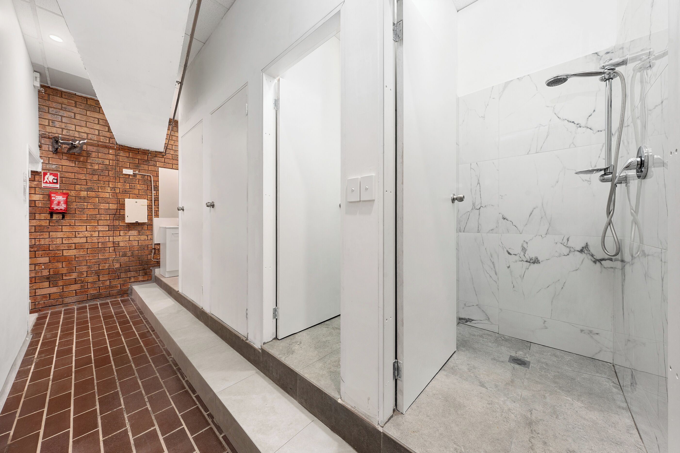 A corridor with a brick wall, white doors, and a shower area with marble tiles.