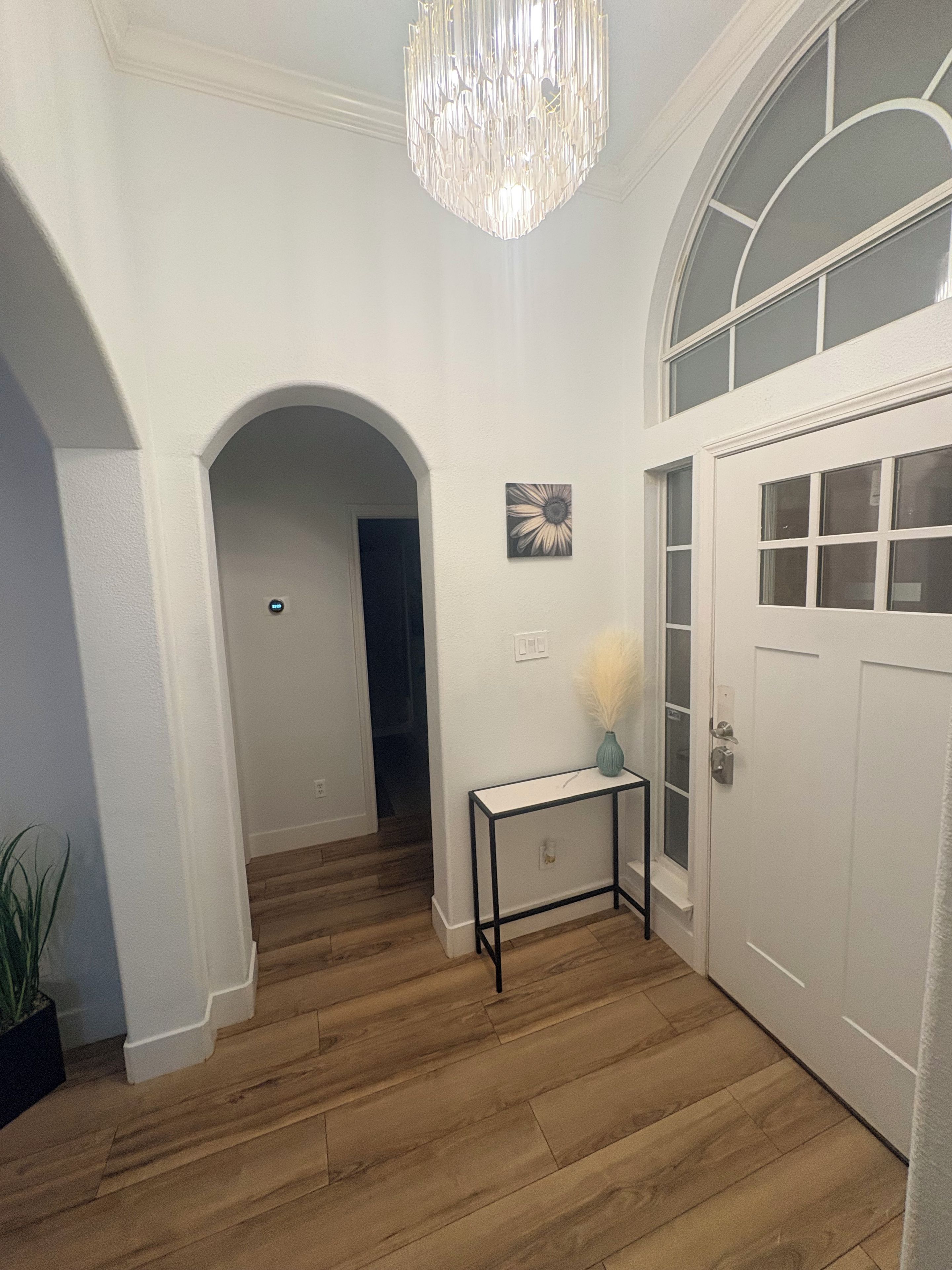 A hallway with wooden flooring, a white door, and a chandelier.