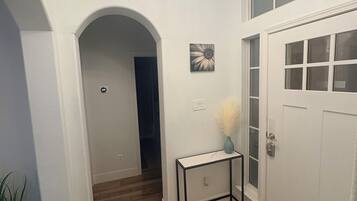 A hallway with wooden flooring, a white door, and a chandelier.