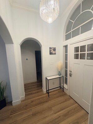 Un pasillo con piso de madera, una puerta blanca y un candelabro.
