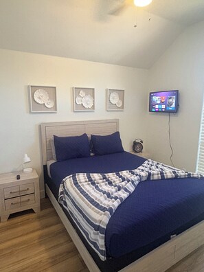 Un dormitorio con cama, mesitas de noche, televisor de pared y cuadros enmarcados.