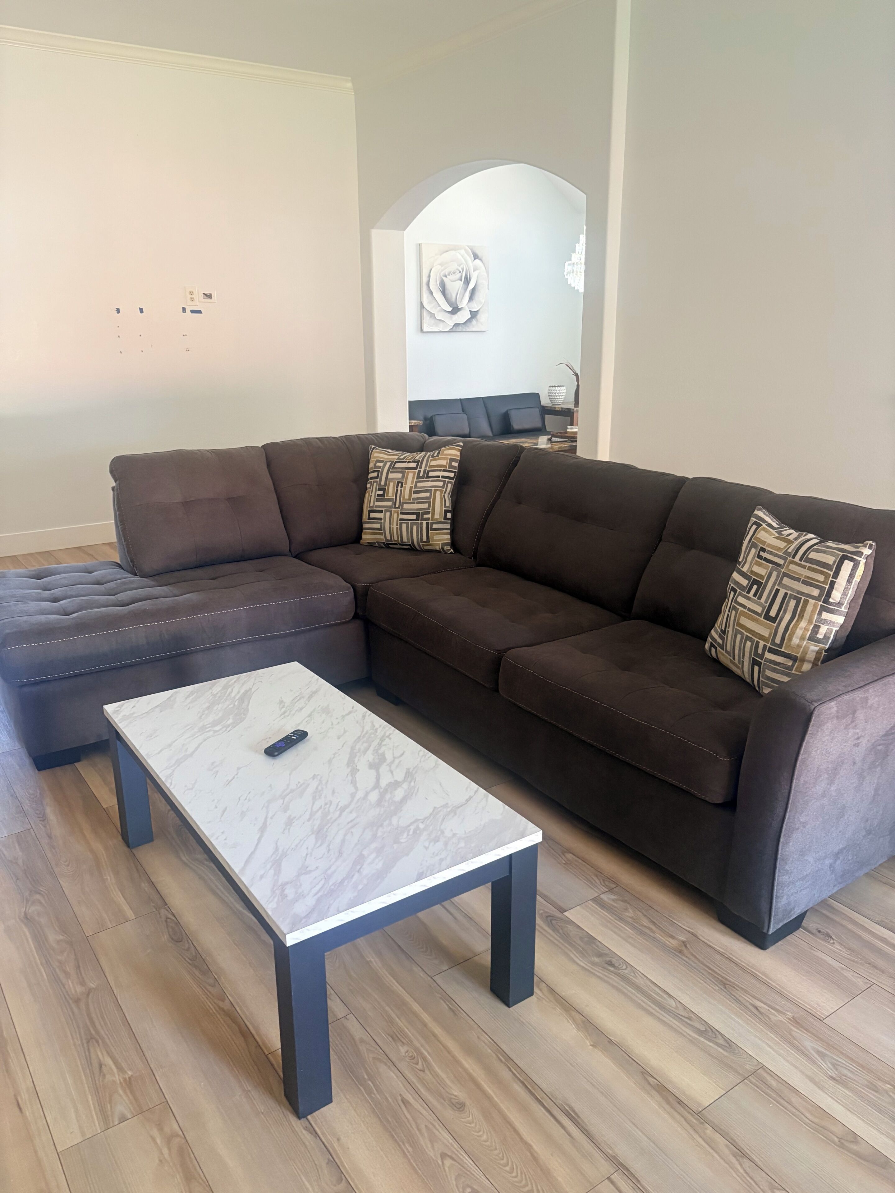 A modern living room with a sectional sofa, ottoman, and a marble coffee table.