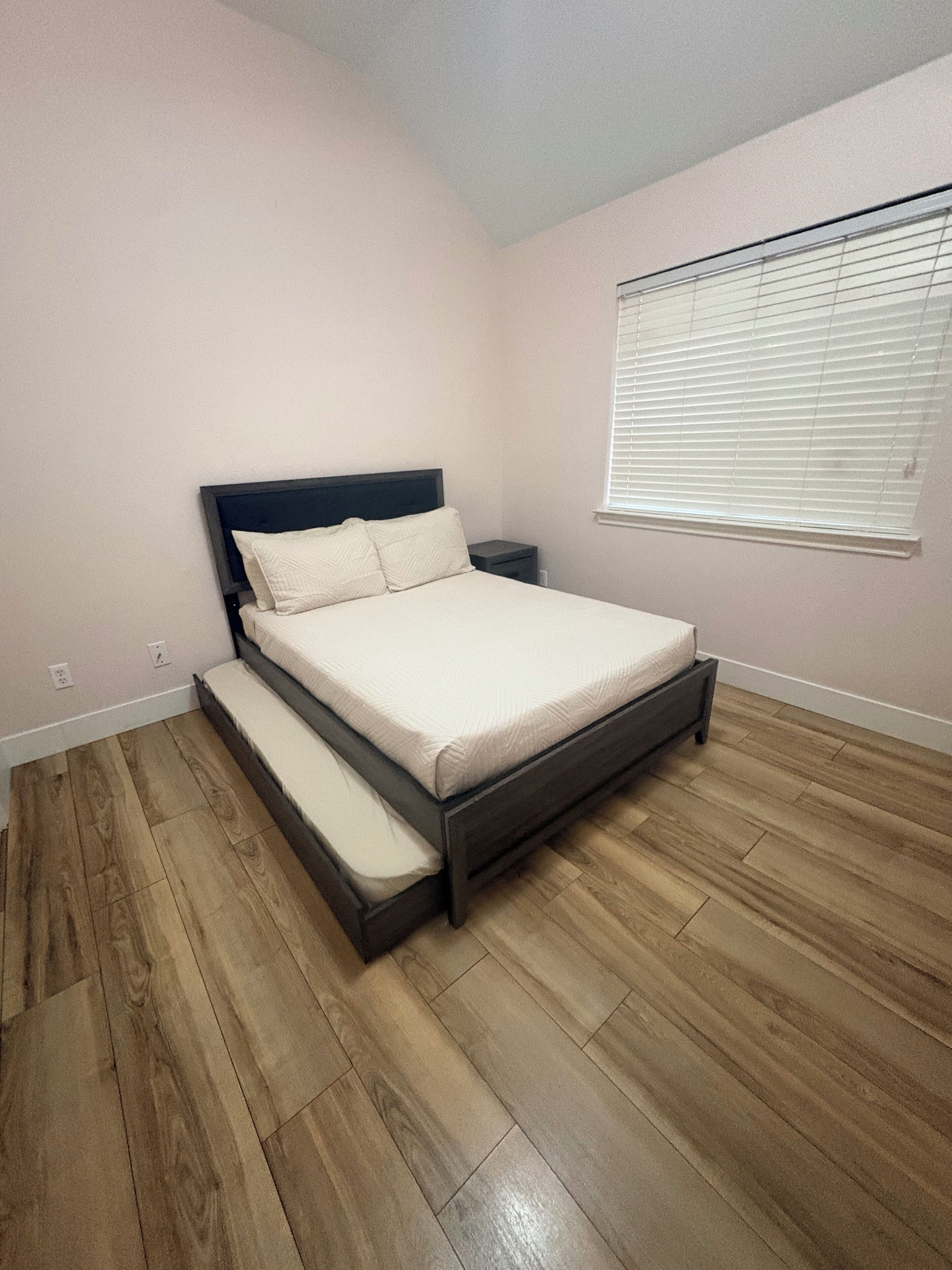 A bedroom with a bed, a nightstand, and a window with blinds.