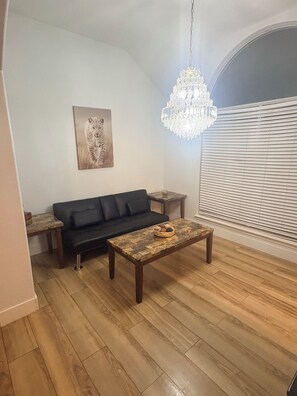 Una sala de estar con un sofá negro, una mesa de centro de madera, una araña y una obra de arte con estampado de leopardo en la pared.