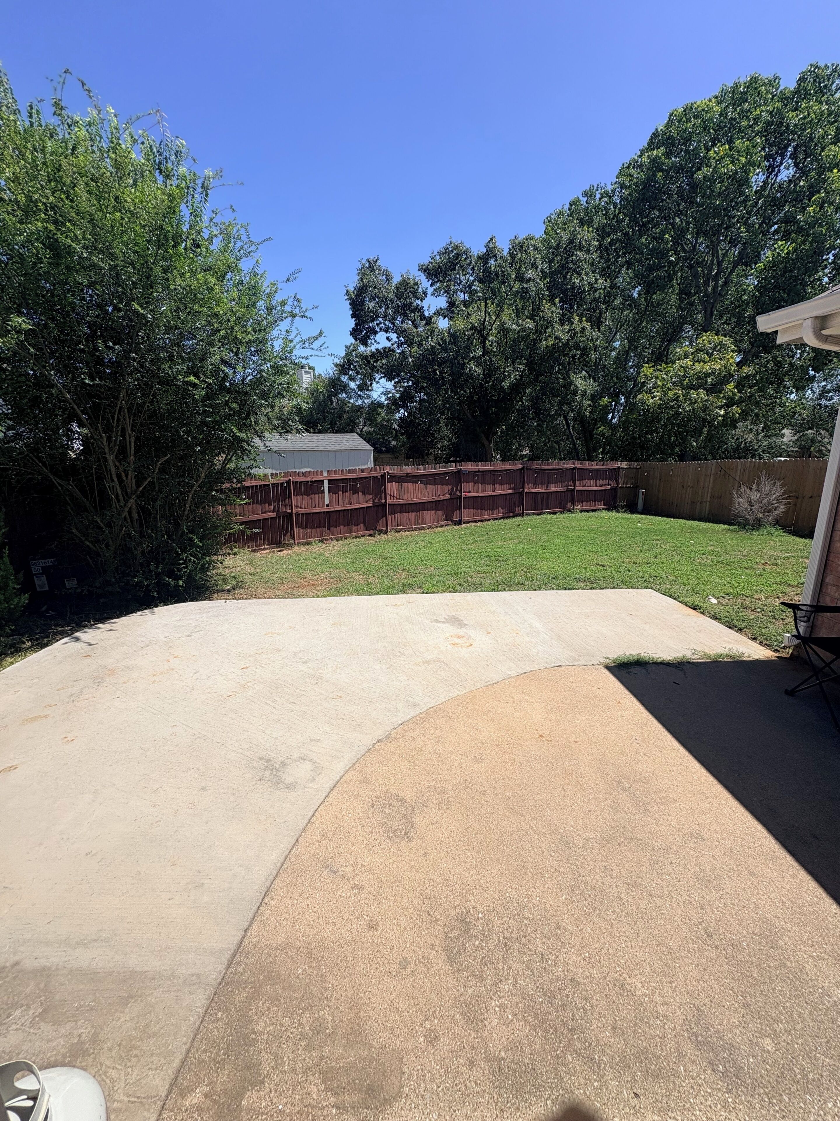 A backyard with a concrete patio, a wooden fence, and a grassy area.