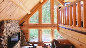 Une cabane dotée d’une cheminée en pierre, de poutres en bois et de grandes fenêtres.