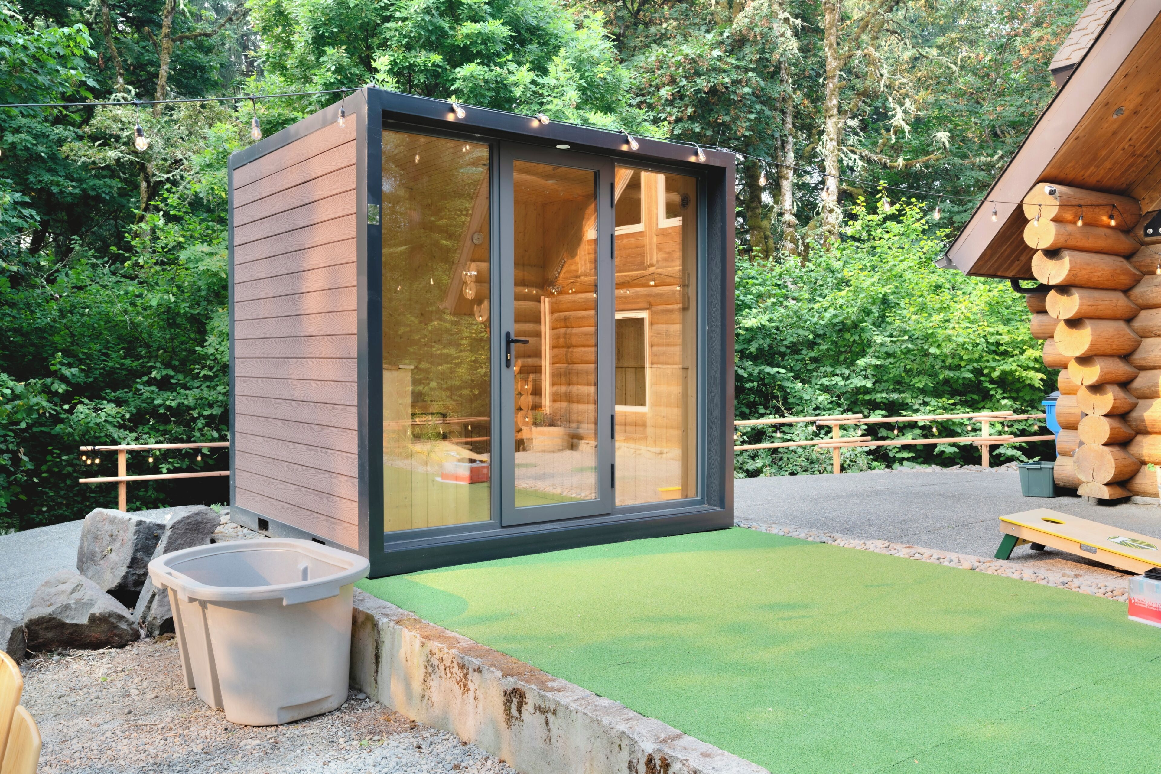 Une cabane en rondins moderne, dotée d’une porte vitrée, d’un petit espace extérieur aménagé pour s’asseoir et d’une terrasse en bois.