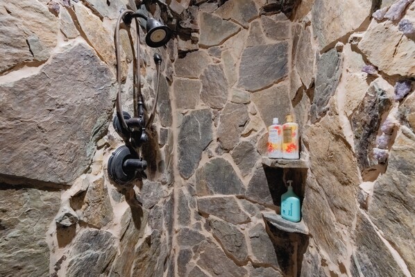 A stone wall with a shower and toiletries.