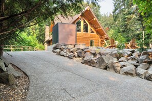 A log cabin with a stone chimney, surrounded by a stone wall and a gravel path leading to it.