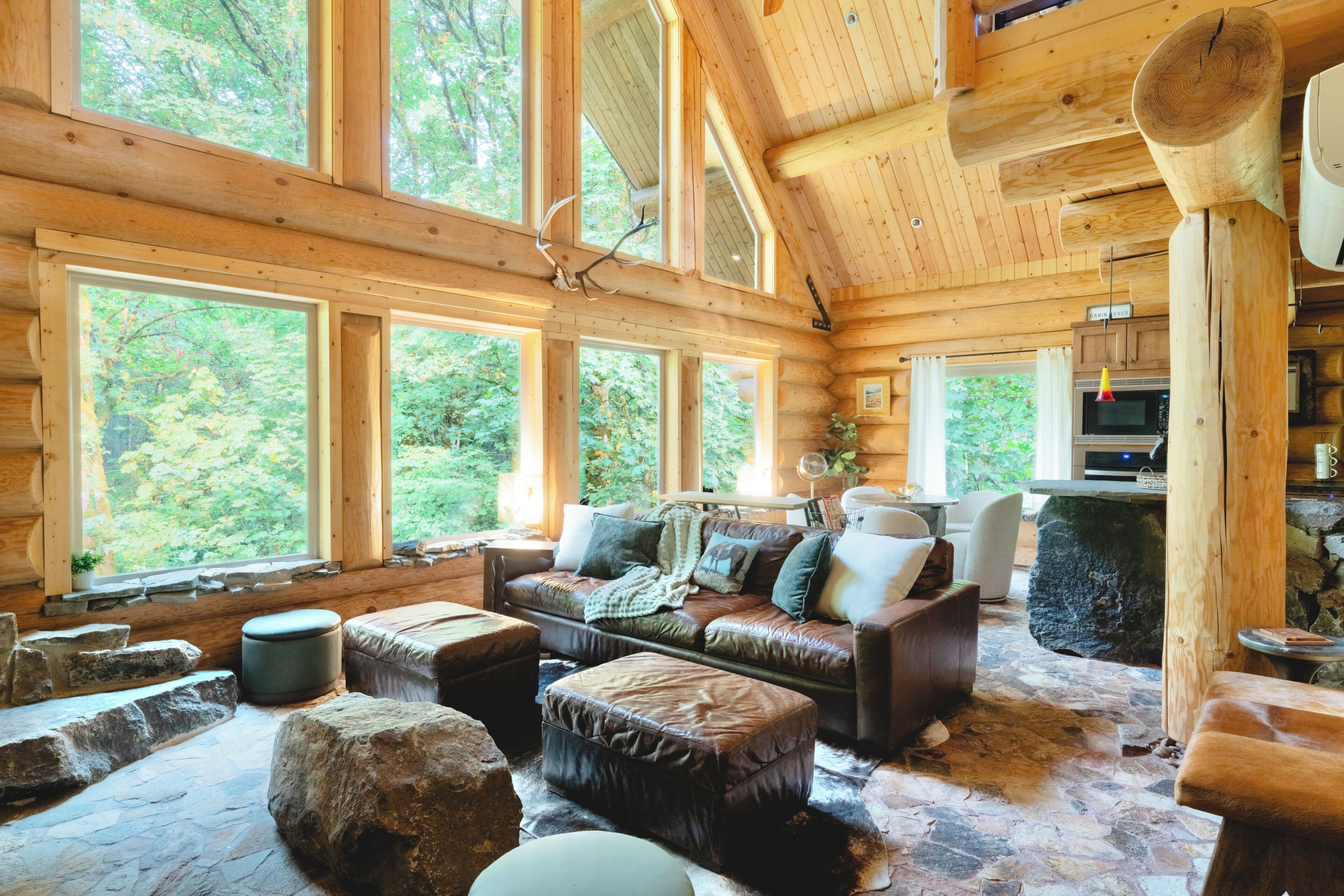 A log cabin interior with a leather sofa, ottomans, and a stone fireplace.