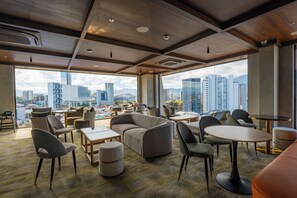 Un hall d’hôtel moderne offrant une vue sur la ville, doté de sièges confortables et d’un aménagement spacieux.
