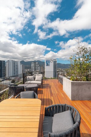 Une terrasse sur le toit, dotée d’une plateforme en bois, de mobilier d’extérieur et offrant une vue sur les bâtiments de la ville et les montagnes.