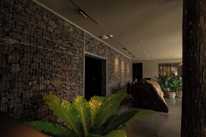 Un hall d’entrée avec un mur en pierre, une grande plante et un banc en bois.