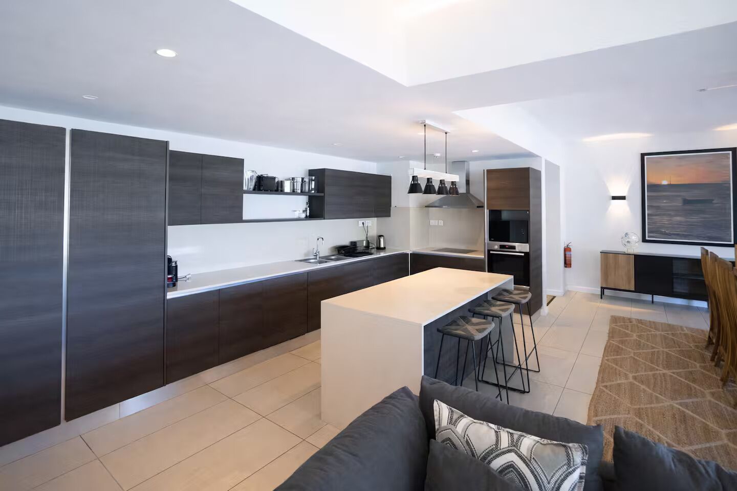 Een moderne keuken met een centraal eiland, donkere kastjes en een eethoek met barkrukken.