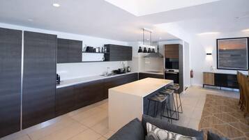 Een moderne keuken met een centraal eiland, donkere kastjes en een eethoek met barkrukken.