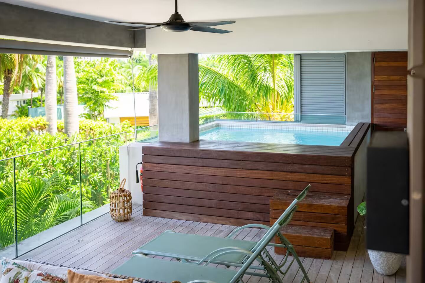 Ein Balkon mit Whirlpool, Deckenventilator und Blick auf üppiges Grün.