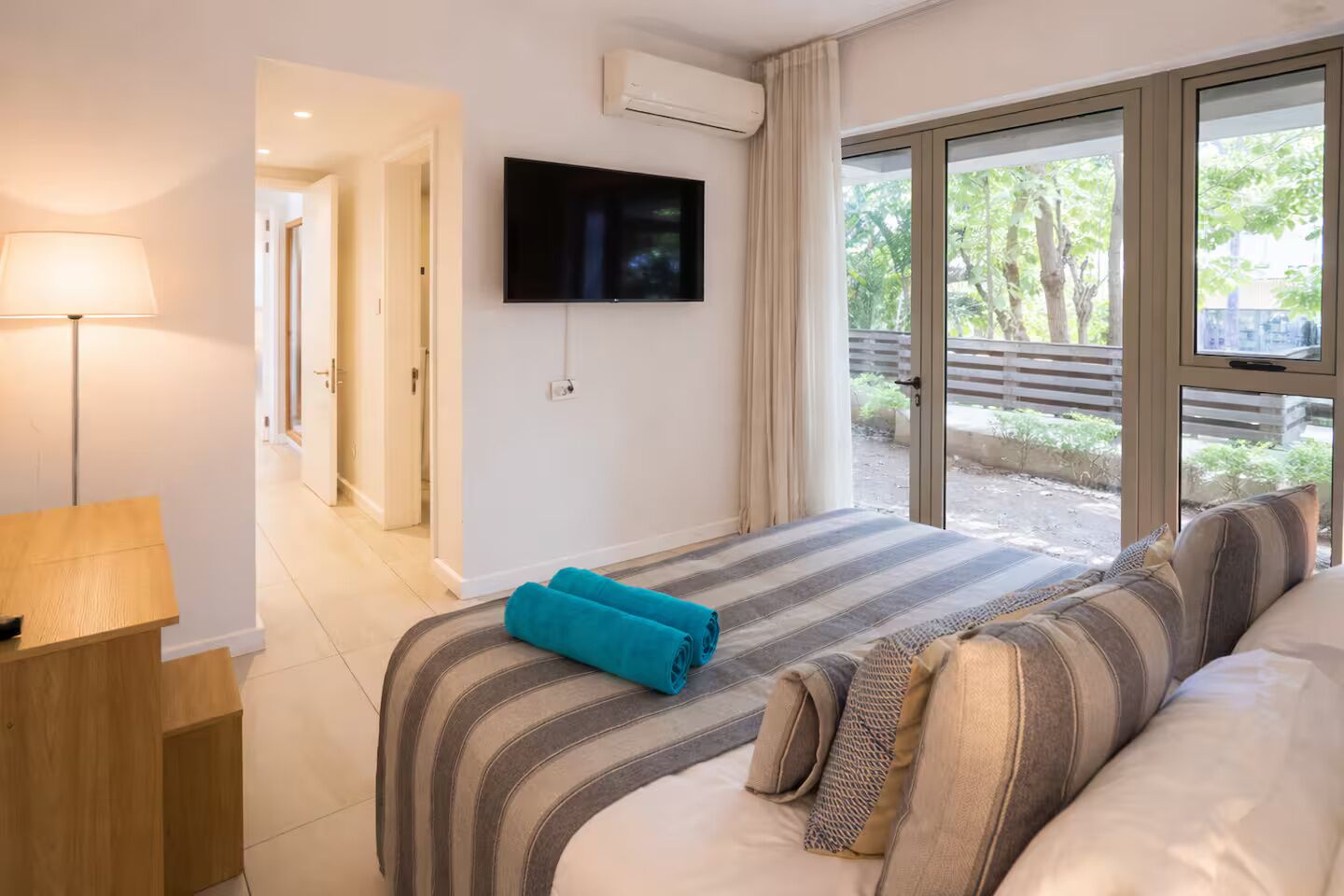 Une chambre d’hôtel avec un lit, un téléviseur fixé au mur, une fenêtre donnant sur un espace verdoyant et une lampe sur une table de chevet.