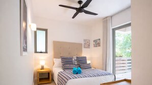 A bedroom with a bed, a nightstand, a ceiling fan, a window, and a view of greenery outside.