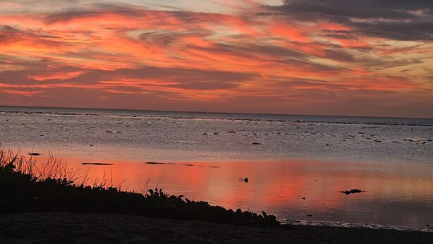 A beach at sunset with a calm sea and a clear sky.