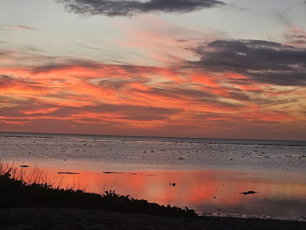 A beach at sunset with a calm sea and a clear sky.