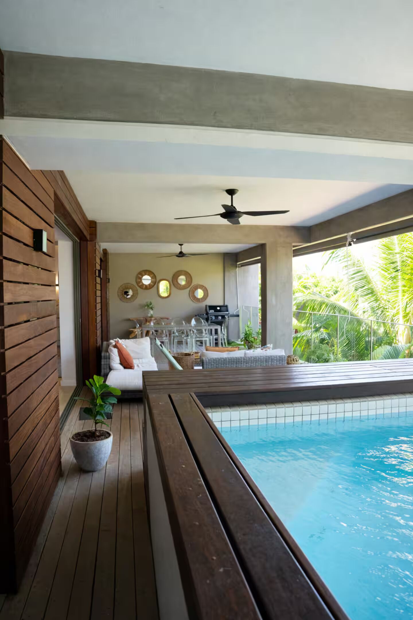 A modern poolside area with a wooden deck, a ceiling fan, and a view of the pool.