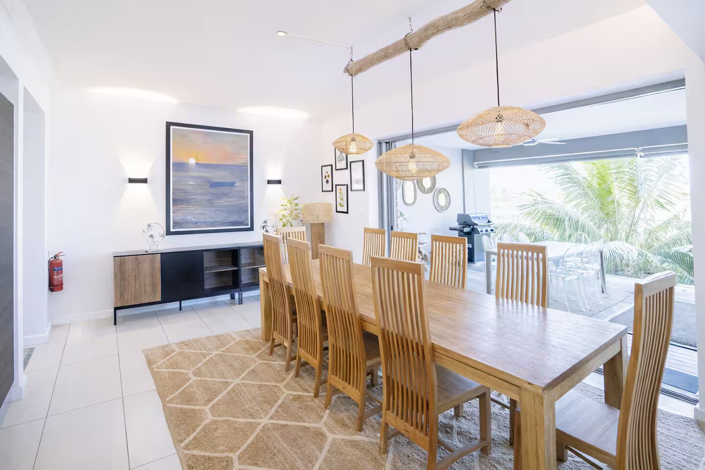 Un espace repas moderne avec une grande table en bois, plusieurs chaises et des lampes en osier suspendues au plafond.