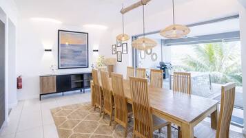 Un espace repas moderne avec une grande table en bois, plusieurs chaises et des lampes en osier suspendues au plafond.