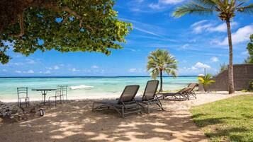 A beach with lounge chairs, a table, and a palm tree.