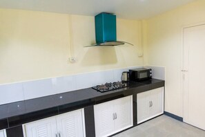 A kitchen with a black countertop, white cabinets, a teal range hood, a microwave, and a gas stove. - 4-bedroom bungalow in tranquil setting (Tambon Choeng Thale)
