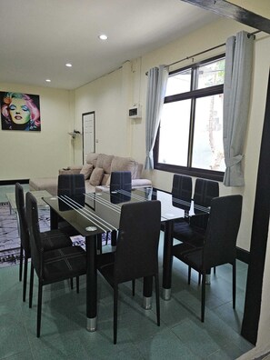 A dining area with a glass-top table, black chairs, a sofa, and a window with curtains. - 4-bedroom bungalow in tranquil setting (Tambon Choeng Thale)