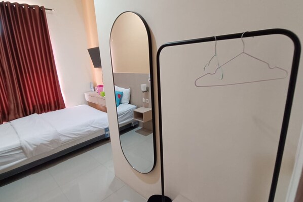 A hotel room with a single bed, a bedside table with a lamp, a mirror, and a coat rack with a hanger.
