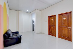 Un hall d’hôtel avec un canapé en cuir noir, deux portes en bois et un sol carrelé.