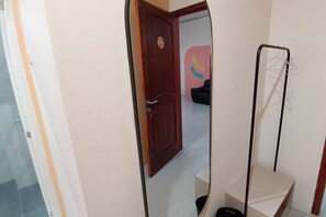 A room with a wooden door, a mirror, a black chair, and a clothing rack.