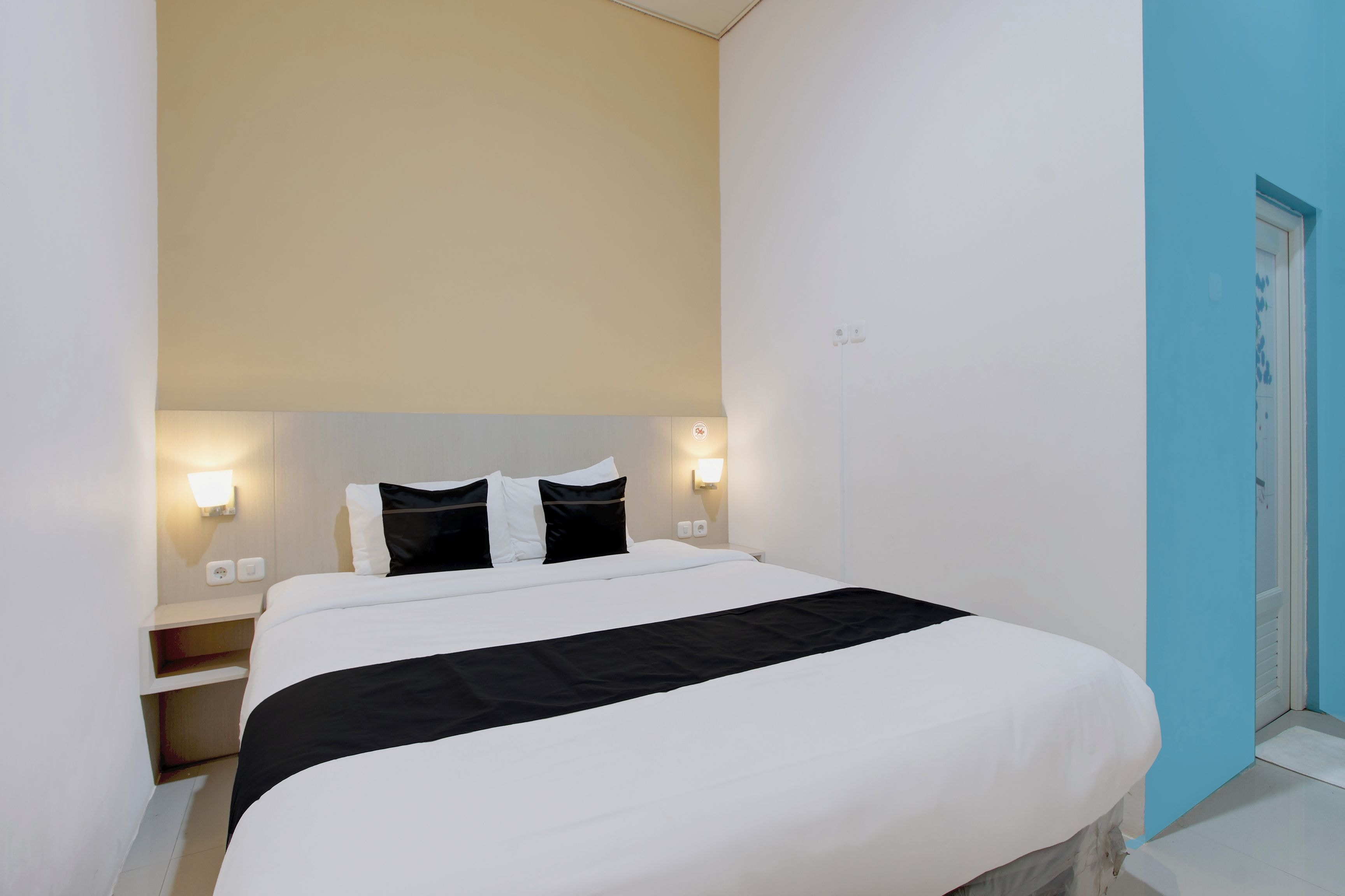 Una habitación de hotel con una cama, lámparas de noche y una puerta.
