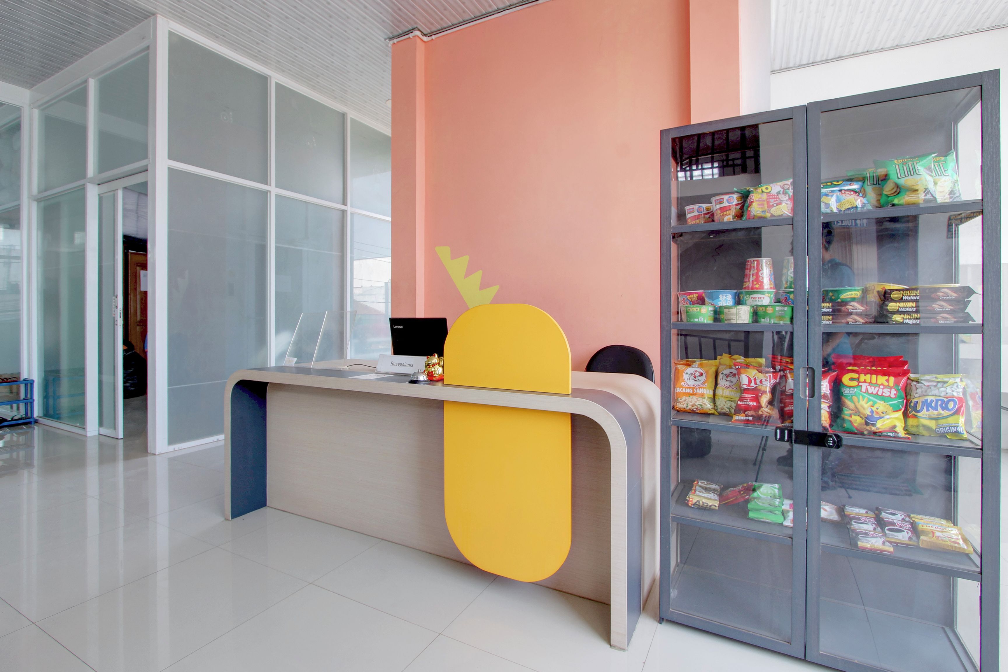 A reception desk with a laptop, a glass cabinet with snacks, and a reception area with a glass wall.