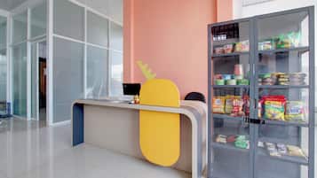 Un mostrador de recepción con una computadora portátil, un aparador con aperitivos y una zona de recepción con pared de vidrio.