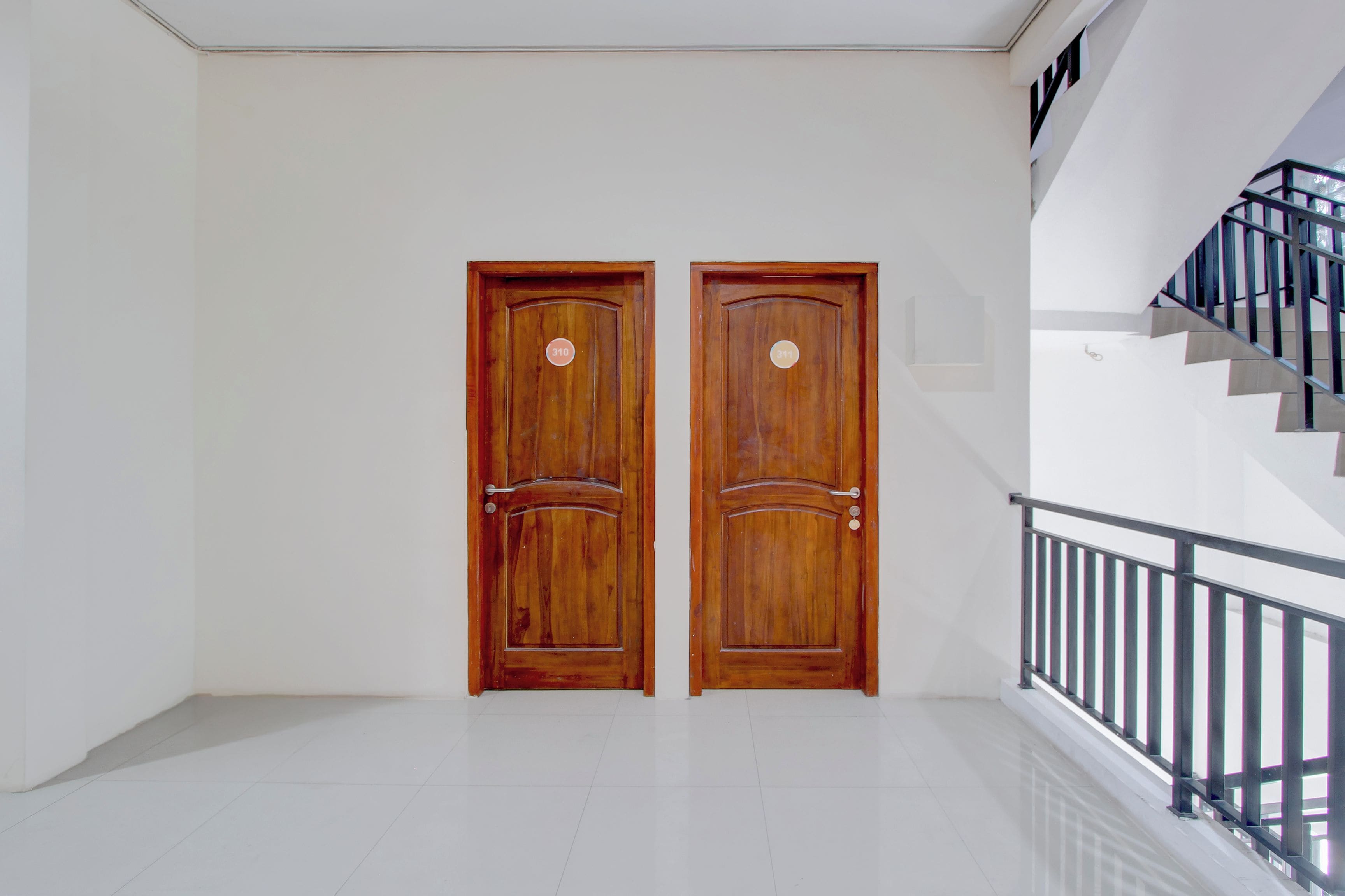 Un par de puertas dobles de madera con una placa de número, una escalera con barandilla de metal y un suelo de baldosas blancas.