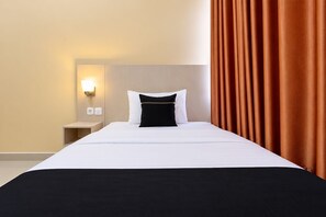 A hotel room with a bed, a nightstand, a wall-mounted light, and a curtain.
