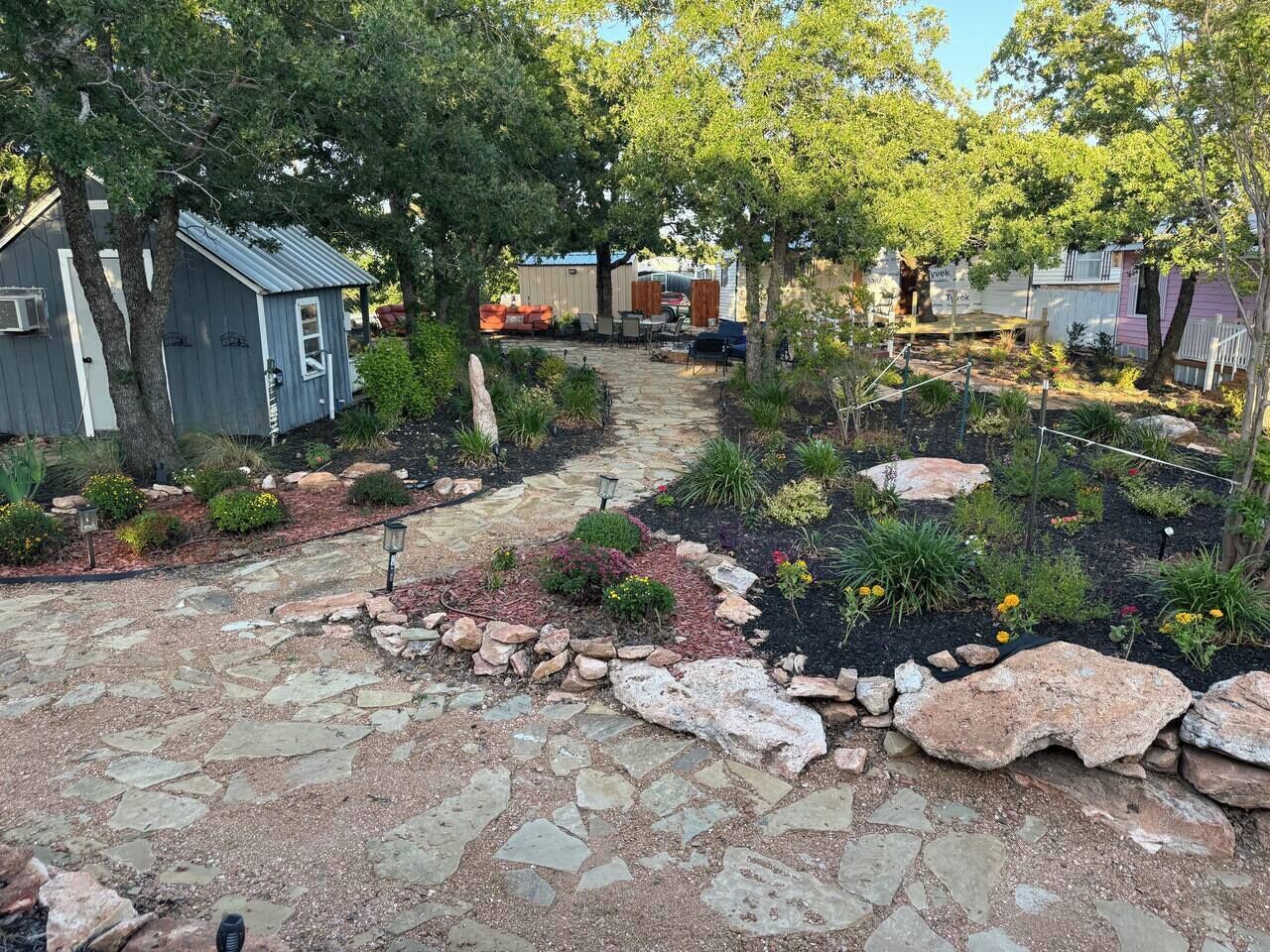 A garden pathway with a mix of stone and gravel, surrounded by various plants and shrubs.