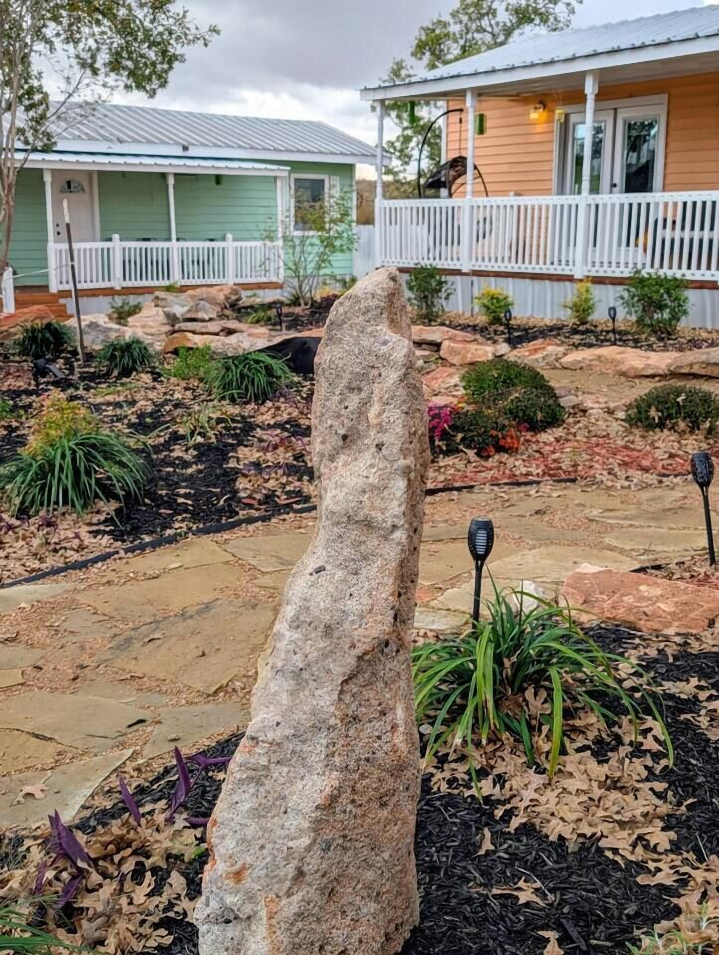 Una construcción de piedra en un jardín ajardinado, con una casa al fondo.