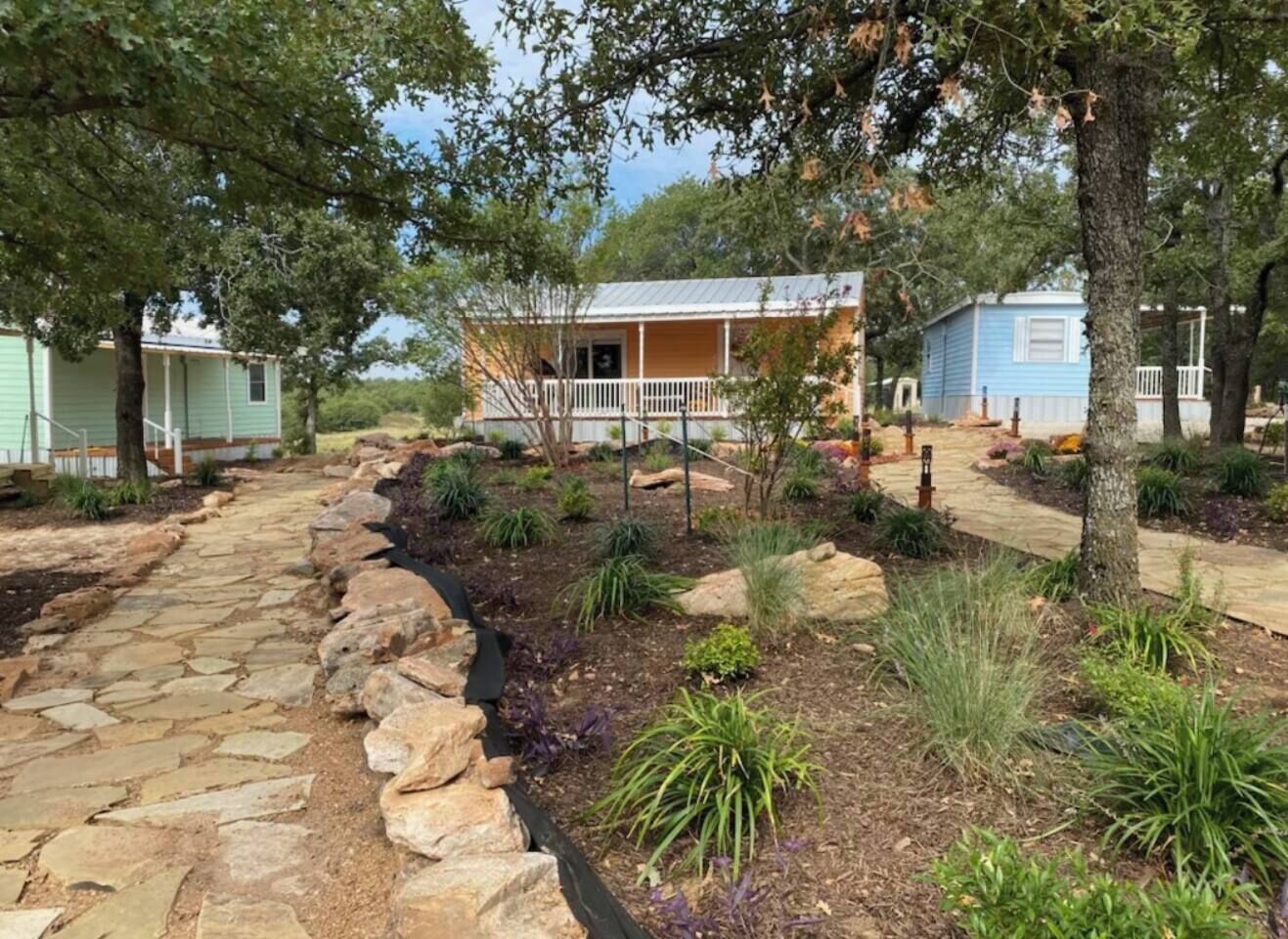 A pathway leading to a house with a porch, surrounded by landscaped garden beds and trees.