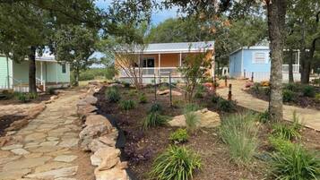 A pathway leading to a house with a porch, surrounded by landscaped garden beds and trees.