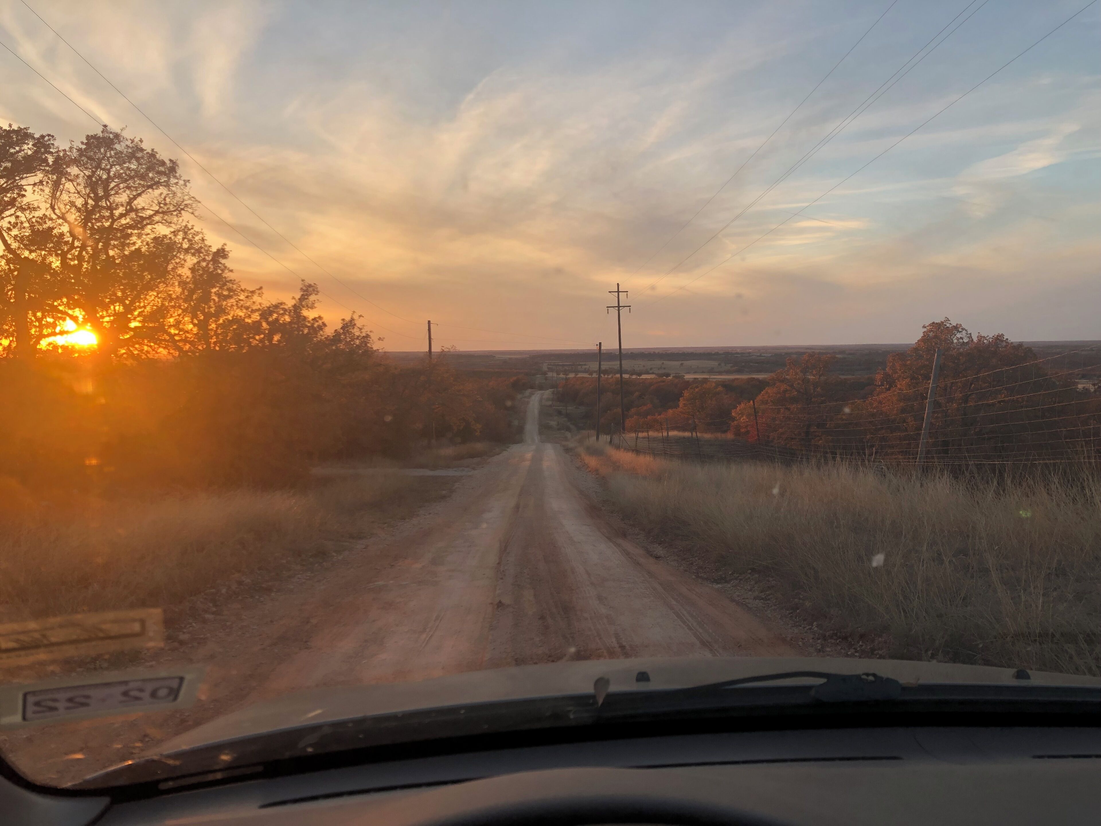 Un camino de tierra que atraviesa un paisaje rural con árboles y líneas eléctricas.