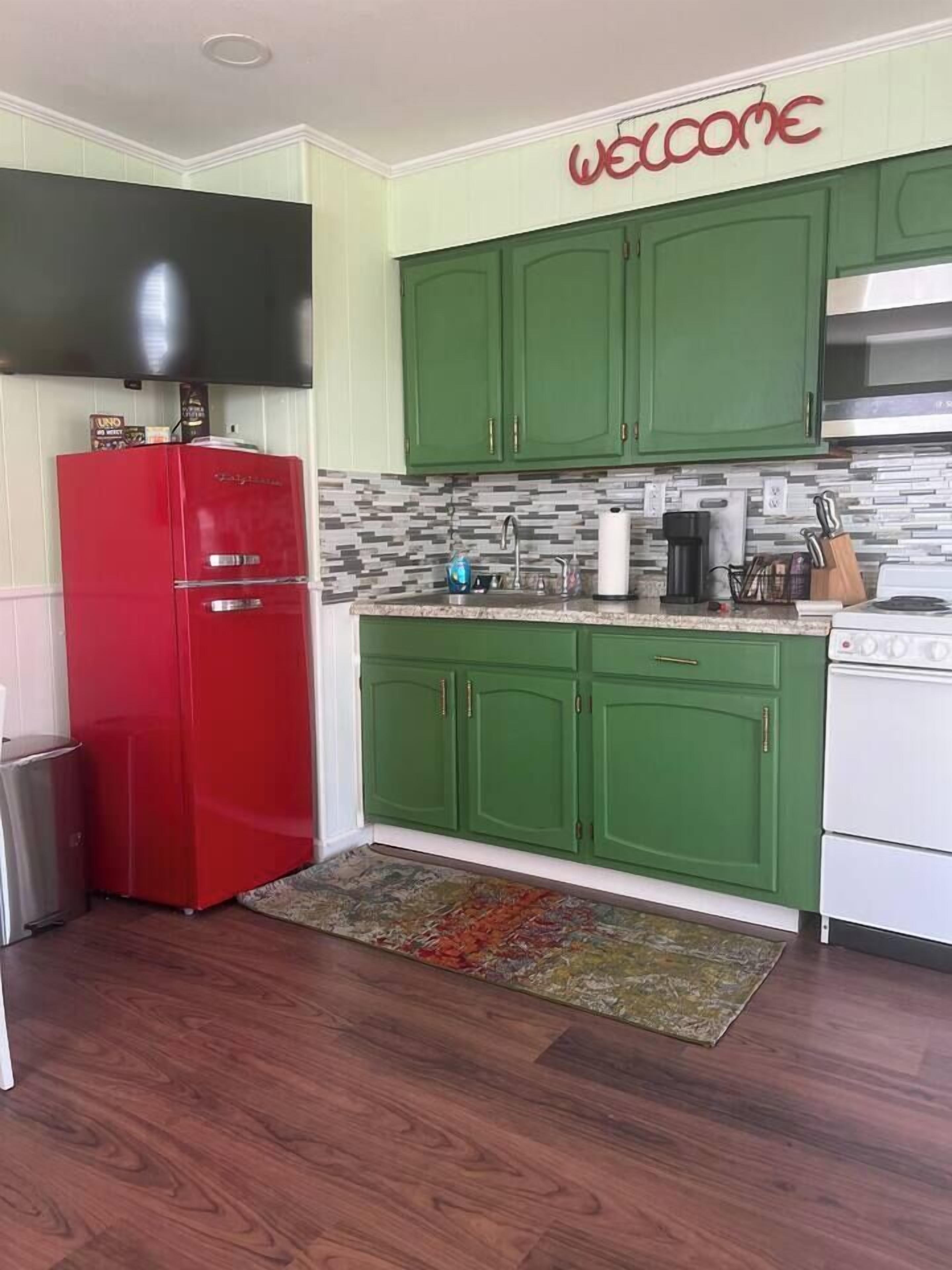 A kitchen with green cabinets, a red refrigerator, and a white stove.