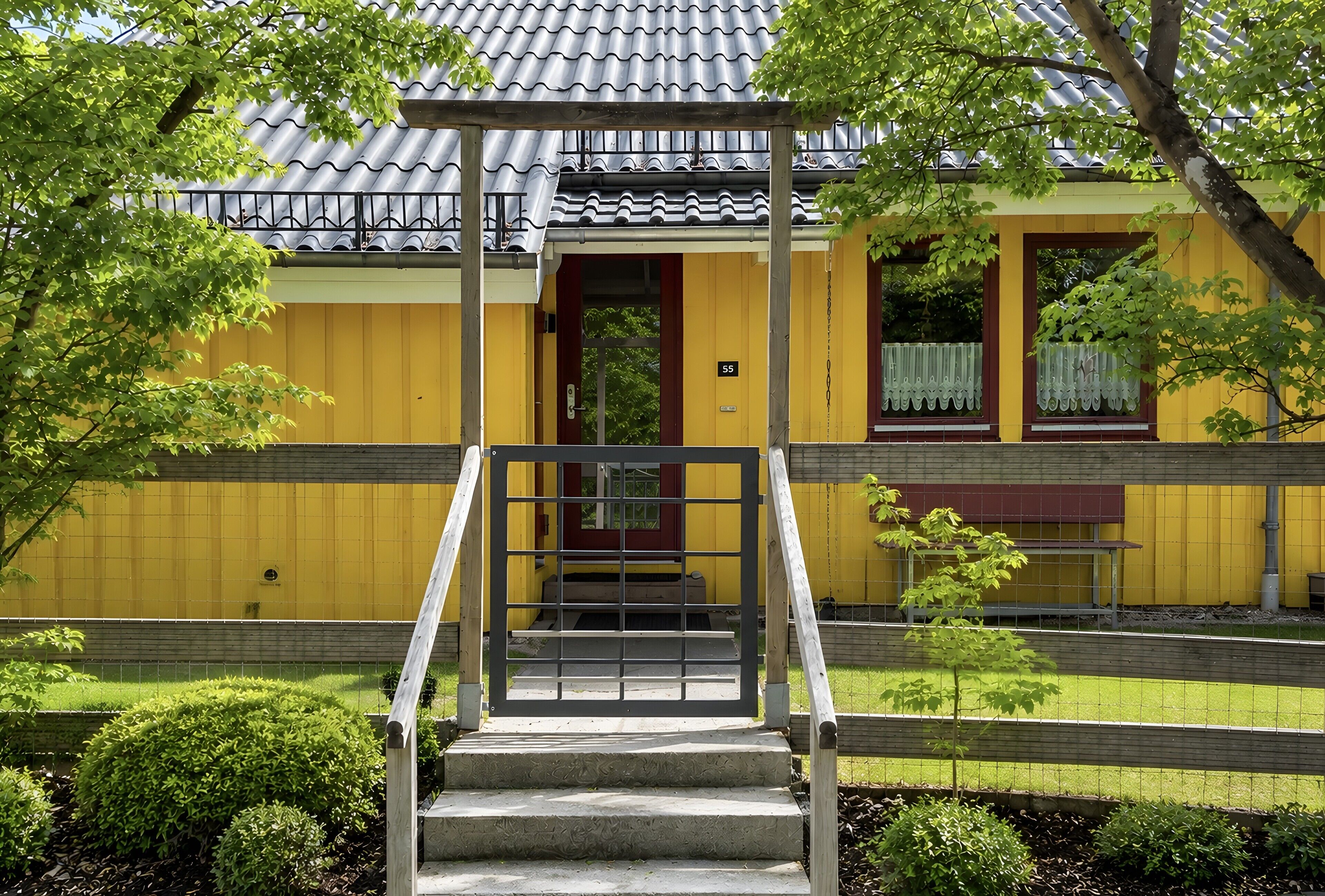 A building with a yellow exterior, a wooden staircase leading to a door, and a small garden area with a bench.