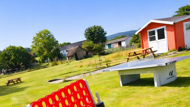 A red and white outdoor seating area with a table and chairs, surrounded by a grassy field and a red building.