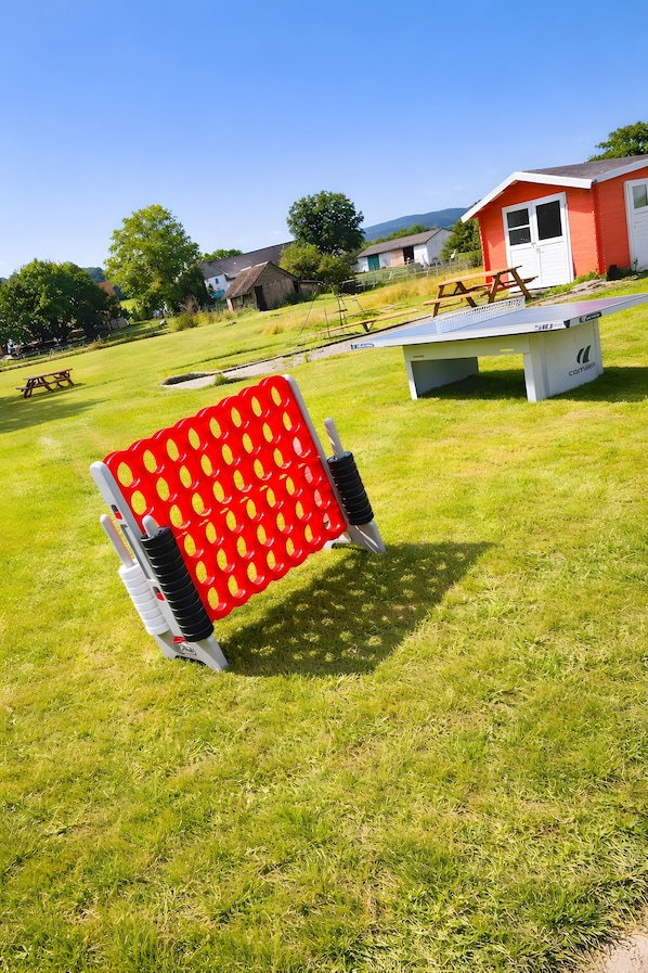 A red and white outdoor seating area with a table and chairs, surrounded by a grassy field and a red building.