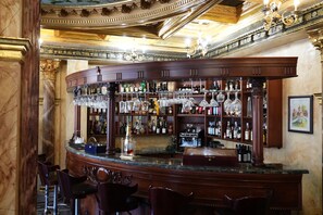 A bar area with a curved counter, shelves of liquor bottles, and hanging glasses. - Alexandrapol Hotel Palace (Gyumri)