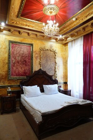 A luxurious bedroom with a large bed, ornate gold detailing, a chandelier, and a red curtain. - Alexandrapol Hotel Palace (Gyumri)